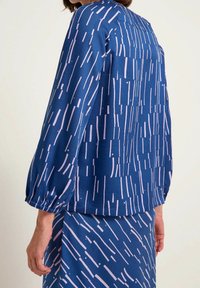 Blå bluse med lyserøde stribemønster, sammenrullede ærmer og en afslappet pasform. Sammen med en matchende mønstret nederdel. Glat stoftekstur.