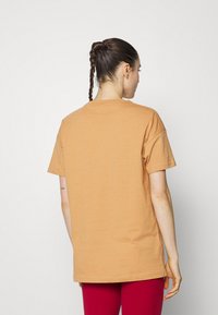 T-shirt de manga curta, de corte largo, em algodão laranja claro. As costas apresentam um decote redondo e um detalhe de costura simples.