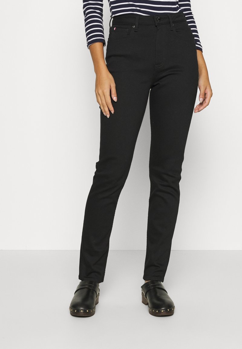 Pantalones negros de talle alto y corte ajustado con una textura suave. Presentan presillas para cinturón, bolsillos delanteros y cierre con botón en la parte frontal.