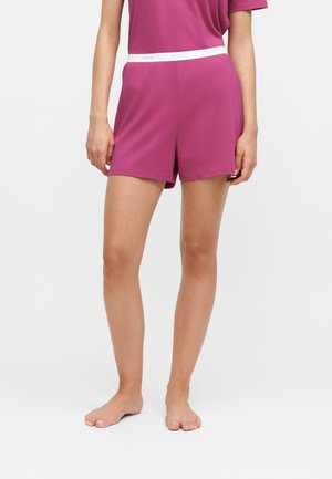 Person wearing pink shorts and a matching pink top, standing barefoot against a plain white background.