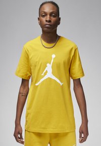 T-shirt in cotone giallo con logo Jumpman bianco. Maniche corte, collo a giro, vestibilità rilassata, con cuciture visibili e texture liscia.