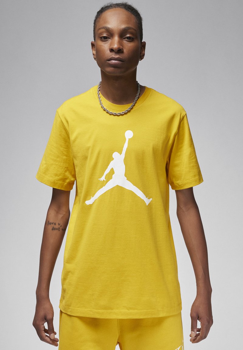 T-shirt in cotone giallo con logo Jumpman bianco. Maniche corte, collo a giro, vestibilità rilassata, con cuciture visibili e texture liscia.