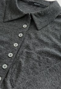 Šedý pletený polo triko s klasickým límcem, šesti knoflíky v předním zapínání s jasnými knoflíky a měkkou texturovanou tkaninou.