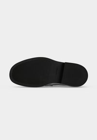 Semelle de chaussure noire avec des parties antidérapantes texturées et le logo Calvin Klein embossé près de la zone de la voûte plantaire sur un fond clair uni.