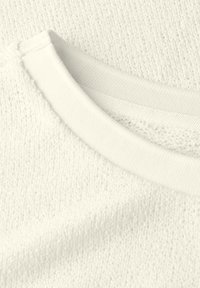 Tissu en tricot blanc avec un col rond et un motif texturé. Le matériau semble doux et légèrement extensible, avec des accents côtelés.