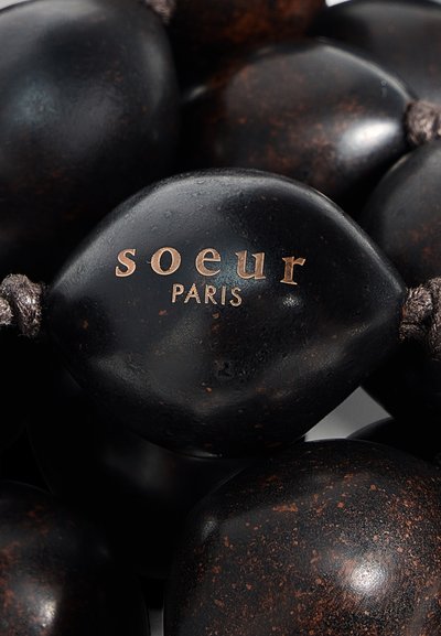 Gros plan d'une perle noire avec un texte doré "soeur PARIS", faisant partie d'un collier texturé noir à perles avec des taches brunes.