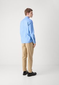 Lichtblauwe overhemd met lange mouwen, beige chino's en zwarte schoenen. Het overhemd heeft een button-down kraag; de chino's zijn recht gesneden met een gladde textuur.