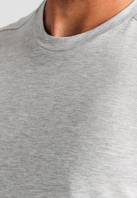 Maglietta grigia a maniche corte con scollo rotondo, caratterizzata da un tessuto morbido, leggermente strutturato e dettagli di cucitura minima lungo il colletto.