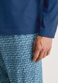 Marineblauwe langemouwen top gecombineerd met blauw patroonbroek met langwerpige vormen, wat een contrast creëert in textuur en kleur.