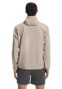 Lekka beżowa kurtka z kapturem, wyposażona w elastyczne mankiety i gładką fakturę. Prosty fason z logo na dolnej części pleców.