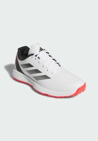 White athletic shoe with black accents and three grey stripes. Features a textured upper and a pink outsole with small spikes for grip.