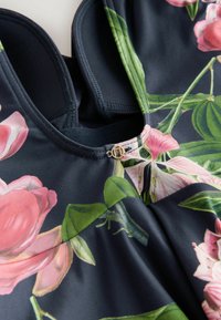Mörk baddräkt med blommönster, med rosa blommor på en marinblå bakgrund, strukturerad tyg och en liten detalj i guld.