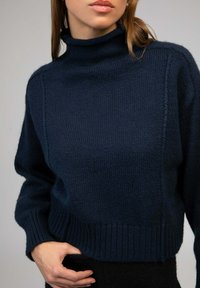 Pull en tricot bleu marine avec col montant, ourlet côtelé et tissu texturé. Dispose d'épaules tombantes et de manches ajustées.