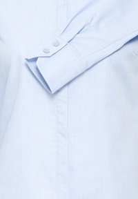 Chemise habillée bleu clair à manches longues pliée avec poignet visible et deux boutons sur le pied de manche.