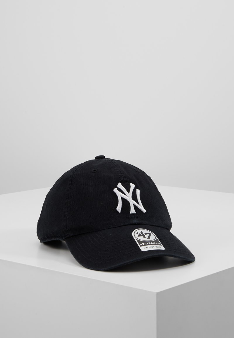 Black cotton baseball cap with white embroidered "NY" logo, curved visor, and adjustable strap. Features a tag on the brim.