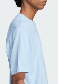 Tricou din bumbac de culoare albastră deschisă, cu guler rotund, mâneci scurte și cusături curate. Prezintă o croială lejeră și o textură moale.