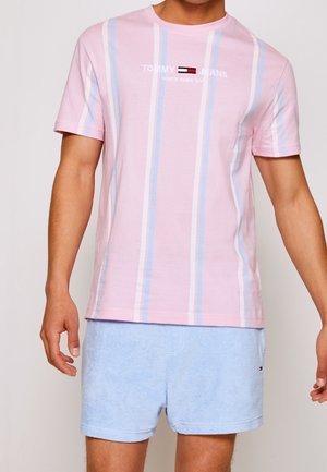 Mężczyzna ubrany w różowy, krótki rękaw w paski z logo "Tommy Jeans" oraz jasnoniebieskie szorty.