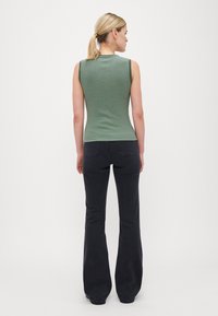 Grønn og marineblå stripete ermeløs topp med en tettsittende design, parret med mørke vide jeans, sett fra baksiden.