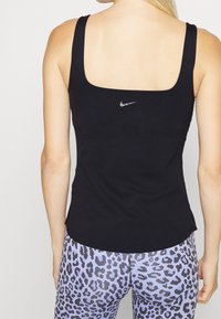 Czarny sportowy top na ramiączkach z kwadratowym dekoltem i cienkimi ramiączkami. Posiada małe srebrne logo Nike na plecach, w połączeniu z legginsami w panterkę.