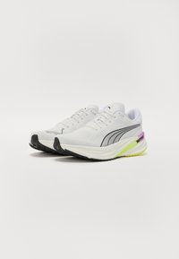 Witte sportieve schoenen met een bovenwerk van mesh, zwarte accentlijnen en een gestructureerde zool. Heeft een groene en paarse hielinzet met het label "NITRO."