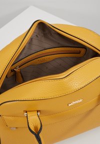 Żółta skórzana torebka z teksturowaną powierzchnią, z kieszenią na zamek, złotymi akcentami oraz podszewką z delikatnymi wzorami.