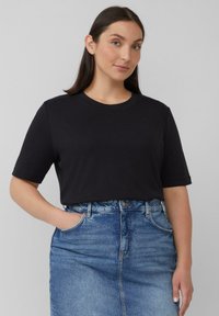 Schwarzes Baumwoll-T-Shirt mit kurzen Ärmeln und rundem Ausschnitt, kombiniert mit einem taillierten Jeansrock in heller Waschung. Glatte Textur und lässiges Design.