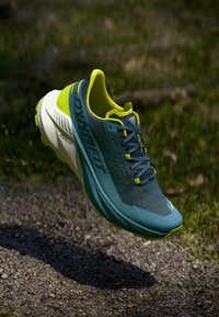 Αθλητικό παπούτσι με υφή μπλε επάνω μέρος, φωτεινές κίτρινες λεπτομέρειες και λευκή σόλα. Διαθέτει κορδόνια και σχεδιασμό με στρογγυλή μύτη.