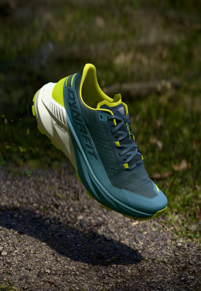 Αθλητικό παπούτσι με υφή μπλε επάνω μέρος, φωτεινές κίτρινες λεπτομέρειες και λευκή σόλα. Διαθέτει κορδόνια και σχεδιασμό με στρογγυλή μύτη.