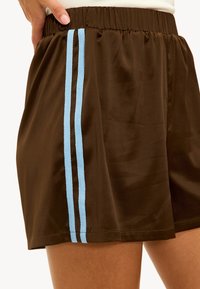 Shorts marron à texture lisse, avec deux bandes verticales bleu clair sur les côtés et une taille élastique pour le confort.