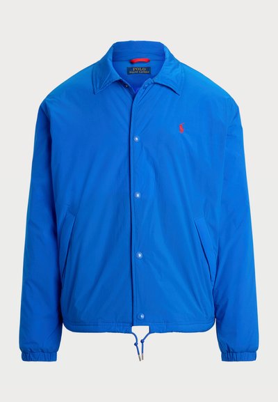 Veste légère bleue avec une fermeture à boutons, des poignets élastiques, un ourlet à cordon et un petit logo rouge sur la poitrine. Fabriquée en tissu lisse.