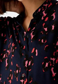 Navy blouse met een leopardenprint in roze en zwart. Heeft een knoopsluiting kraag en zwarte knopen langs de sluiting.