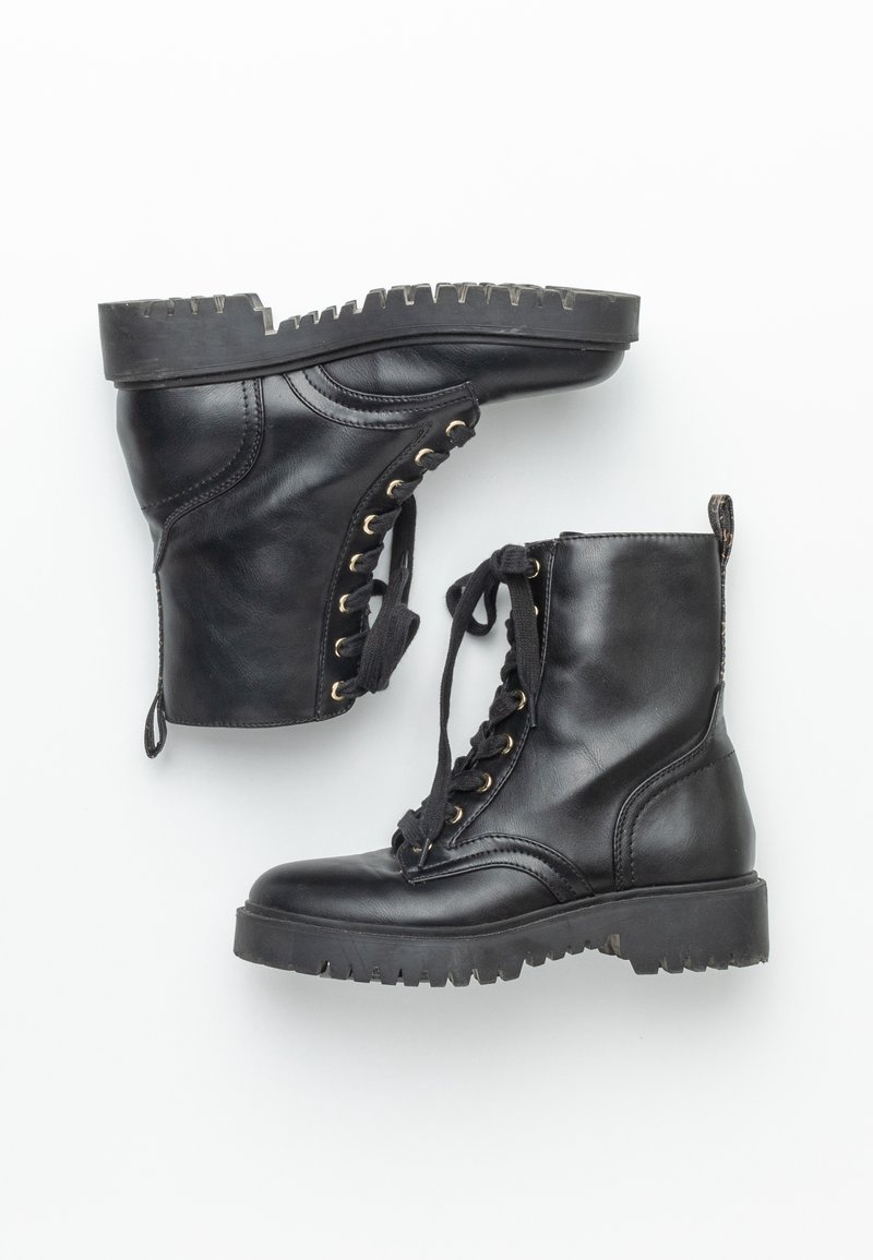 Bottes de combat en cuir noir avec semelles crantées épaisses et lacets noirs, une botte debout et l'autre sur le côté sur fond blanc.