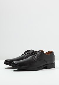 Chaussures de ville en cuir noir avec une texture lisse, bout rond et design à lacets. Présentent un talon bas et des détails de couture subtils.