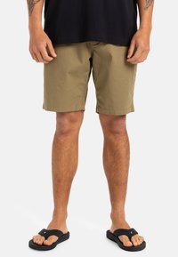 Shorts kaki à coupe décontractée, fabriqués en tissu léger. Portés avec des tongs noires. Coutures visibles et design simple.