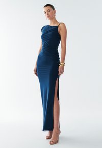 Noční šaty námořnické modré barvy s nařasenou texturou, asymetrickým střihem přes jedno rameno a vysokým rozparkem přes stehno. Mají tenké ramínka a přiléhavý střih.