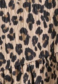 Leoparda raksta audums ar bēša fonu un melnām plankumiem, ar teksturētu, krokotā raksta un slāņveida dizaina elementiem.