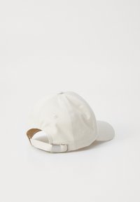 Bomuldsbaseballcap i off-white med buet skygge og justerbar rem bagpå med metalspænde. Glat, blød tekstur.