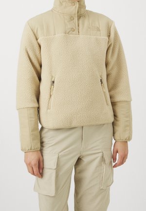 Pullover in pile beige con colletto alto, chiusura a scatto e due tasche laterali con zip. Tessuto morbido e testurizzato con pannello superiore in contrasto.