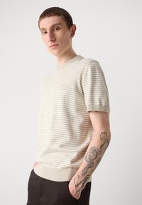 Beige svītrains īsām piedurknēm džemperis ar ribotām piedurknēm un apakšmalu, piedāvājot mazu logo uzrakstu uz krūts un gludu teksturētu audumu.