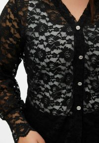 Zwarte kanten blouse met bloemmotieven, lange mouwen, een knoopsluiting aan de voorkant met doorzichtige, decoratieve knopen en een getextureerd oppervlak.