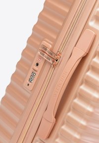 Roze gouden koffer met ribbelontwerp, ritssluiting, cijferslot en gegraveerde merknaam. Gelaagd oppervlak voegt visuele interesse toe.