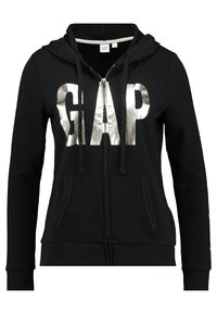 Sudadera con cremallera negra hecha de tela suave, que presenta un gran logotipo metálico plateado "GAP" en el frente, con capucha y bolsillos frontales.