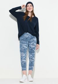 Marinblå långärmad topp i kombination med åtsittande blå mönstrade leggings med vågiga mönster och djurtryck, kompletterat med vita sneakers.