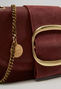 Sac à main en cuir et daim bordeaux avec bandoulière chaîne dorée et grande boucle dorée sur le rabat.