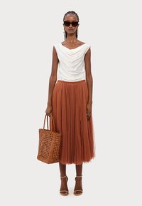Top bianco drappeggiato, gonna midi in tulle ruggine, borsa a spalla intrecciata marrone, décolleté marroni con cinturini, occhiali da sole neri oversize e orecchini dorati.