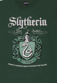 Zelené bavlněné tričko s erbem Slytherinu, které obsahuje hada, ornamentální detaily a bílý text "Slytherin Team Quidditch."
