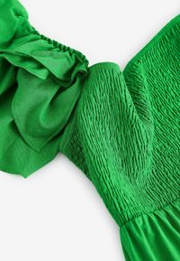Détail d'une robe verte avec des manches volantées, une texture de corsage froncé et une jupe fluide. Tissu lisse de couleur vive et unie.