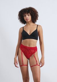 Bralette noire et culotte porte-jarretelles en dentelle rouge avec bretelles réglables, présentant des motifs complexes et un détail de nœud central.
