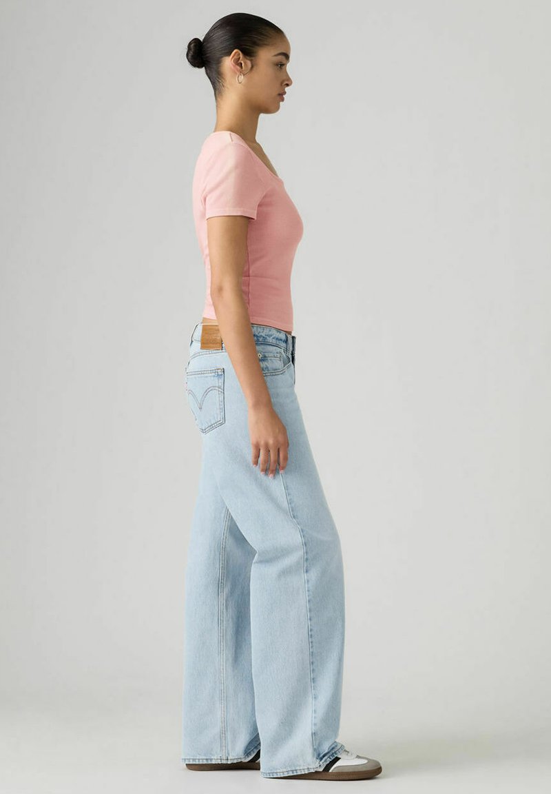 Pink fitted t-shirt and light blue wide-leg jeans. The jeans feature a distinct back pocket design and a tan leather patch on the waistband.