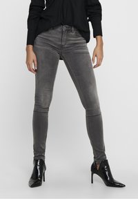 Jeans ajustados grises con una textura suave, que presentan una cintura alta y un ligero desvanecimiento, combinados con botas de tobillo negras con tacón brillante.
